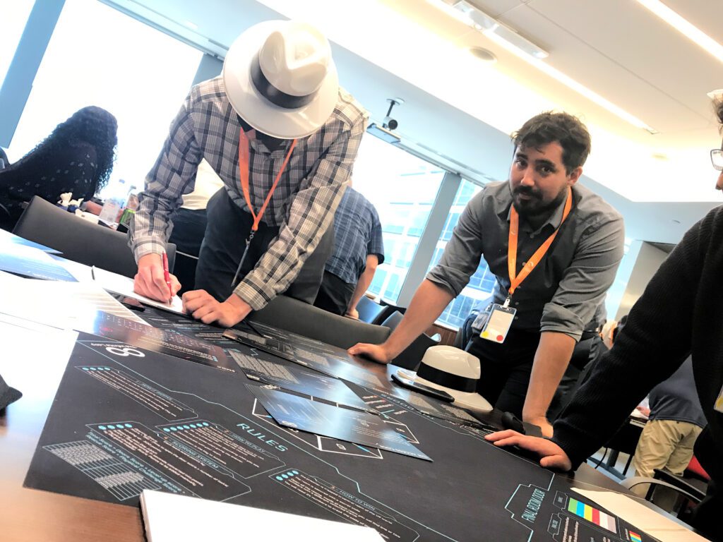 Team members collaborate on solving puzzles during The Infinite Loop team building event, with one participant writing notes and another observing the challenge map.