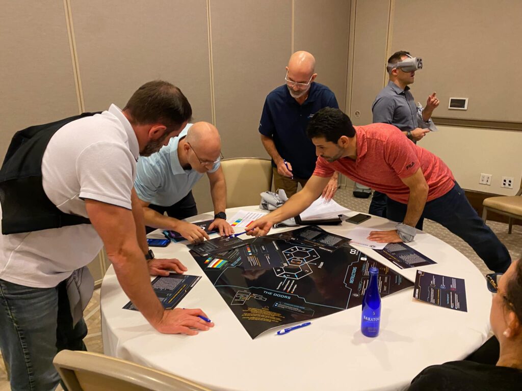 A group of participants works together on a challenge map during The Infinite Loop team building event, while one team member engages with virtual reality.