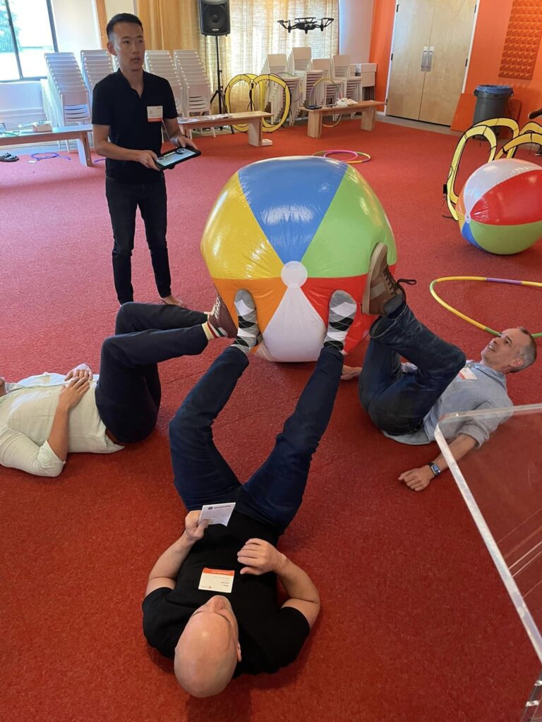 Participants engage in a creative problem-solving challenge during the Game of Drones team building event, using teamwork to maneuver a large beach ball.