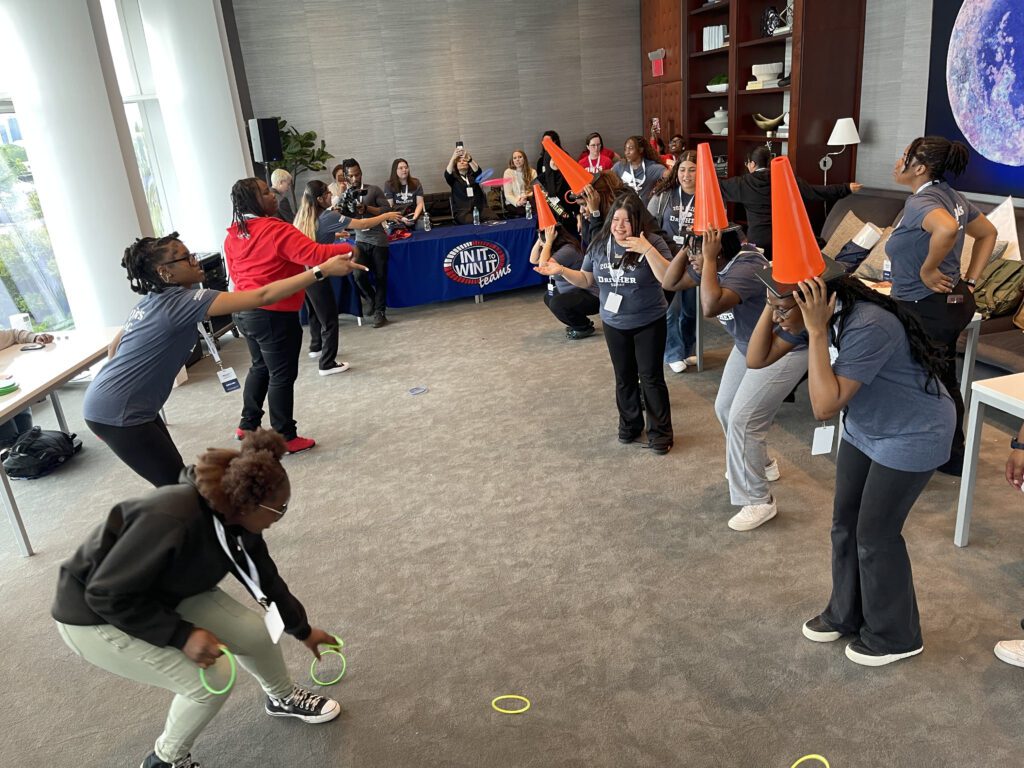 Participants engaged in a lively ring toss challenge, with some wearing traffic cones on their heads as targets, during the In It to Win It team building game, creating a fun and energetic atmosphere.