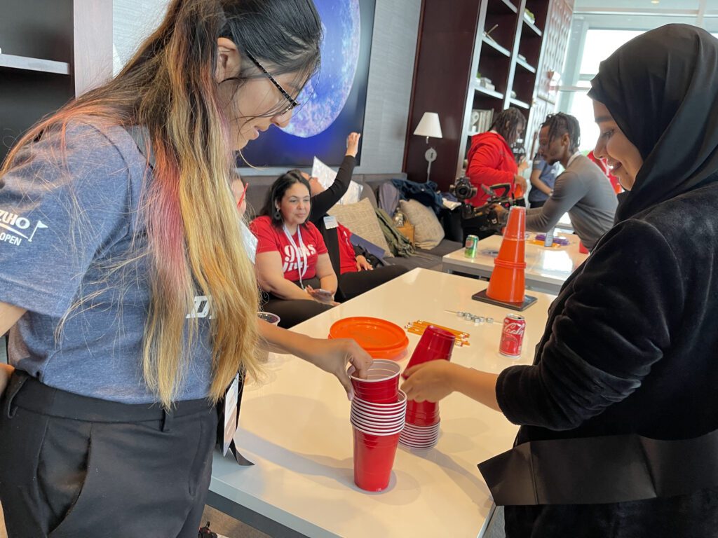 Two participants focused on a cup stacking challenge during the In It to Win It team building activity, displaying teamwork and concentration in a lively and engaging environment.