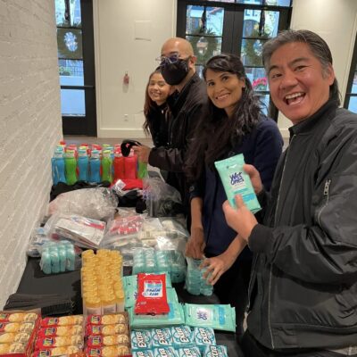 Participants smile while assembling personal care kits during the Helping Hands team building event. They work together to organize hygiene products and snacks for community members in need.