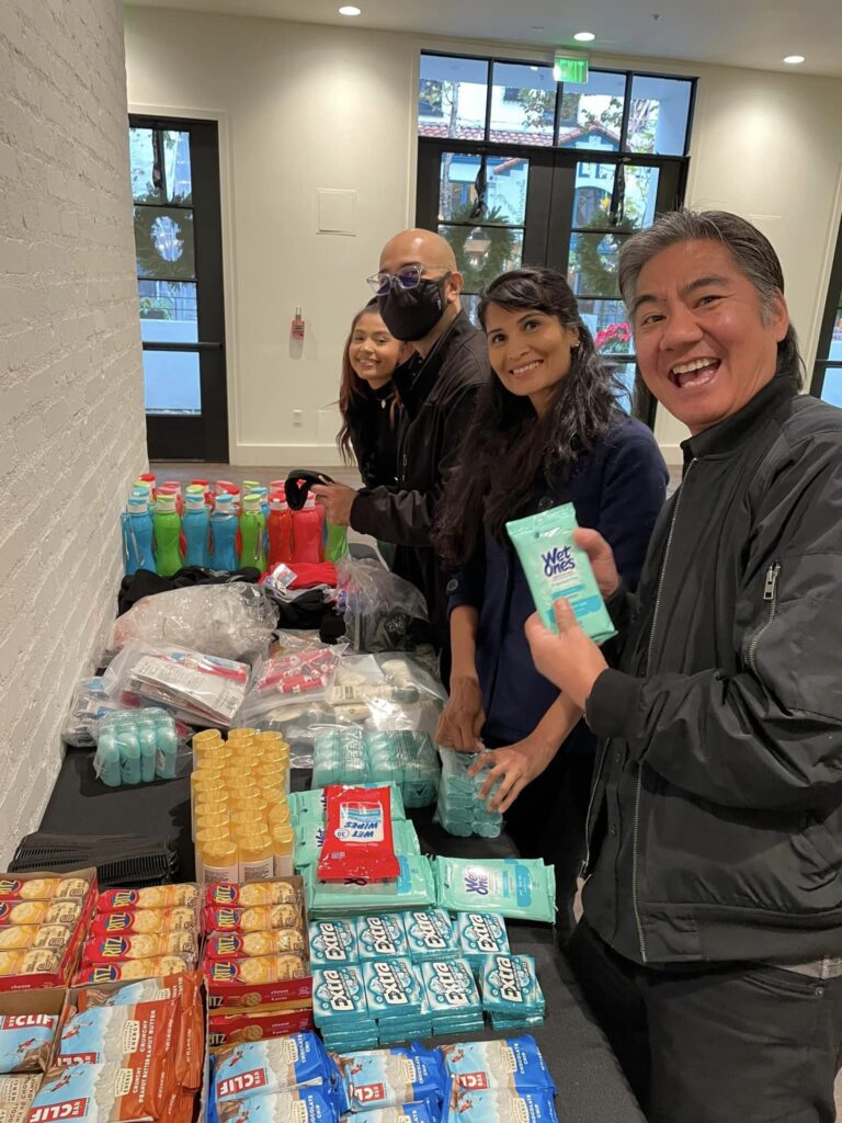 Participants smile while assembling personal care kits during the Helping Hands team building event. They work together to organize hygiene products and snacks for community members in need.