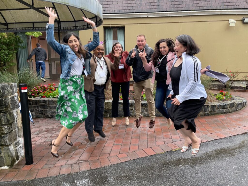 Group of seven team members joyfully jumping in the air during the Healthcare Heroes team building event. Participants, smiling and mid-air, embody the fun and energy of the event aimed at supporting healthcare professionals.