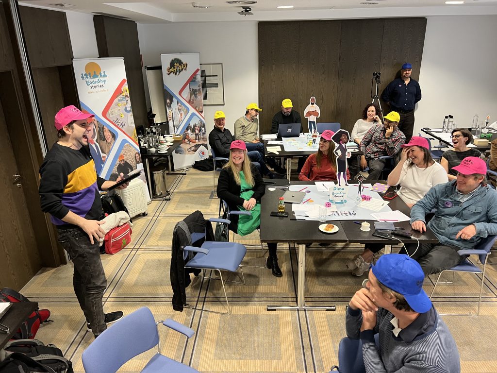 Team members actively participating in the Leadership Stories game, wearing colorful hats and engaging in discussions, creating a fun and interactive learning environment.