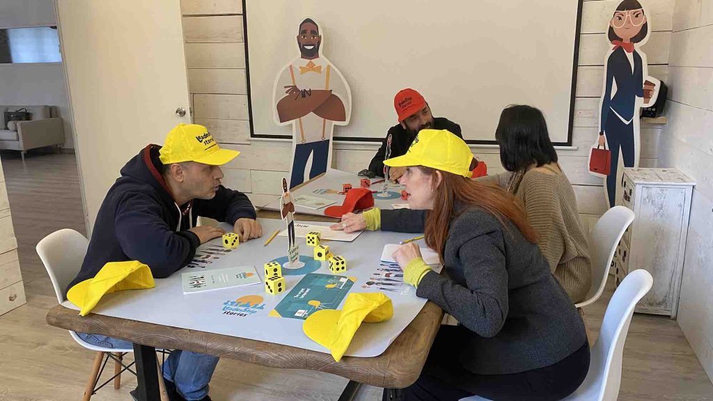 Team members engaging in the Leadership Stories game, wearing yellow hats and playing with game materials like dice and figurines, in a team building environment designed to enhance leadership skills.