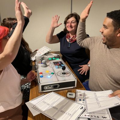 Excited participants high-five during the Team Synergy retro gaming team building activity, celebrating their success and teamwork around a game console.