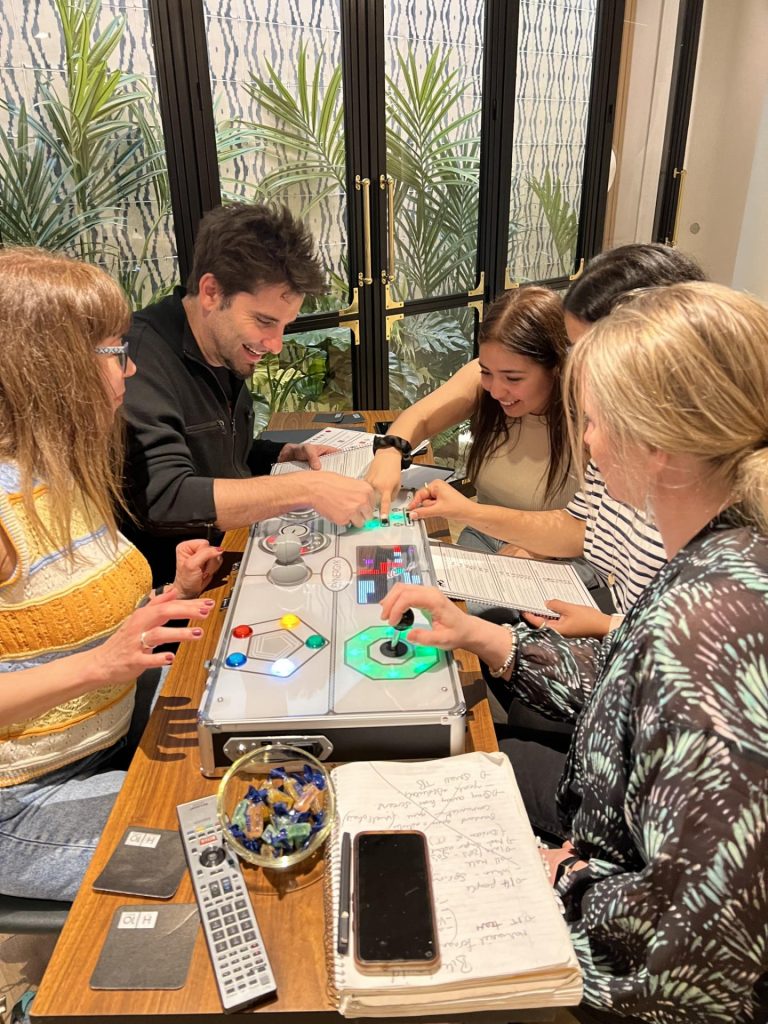 A group of participants working together on a Team Synergy retro gaming console, solving puzzles and collaborating during a team building activity.