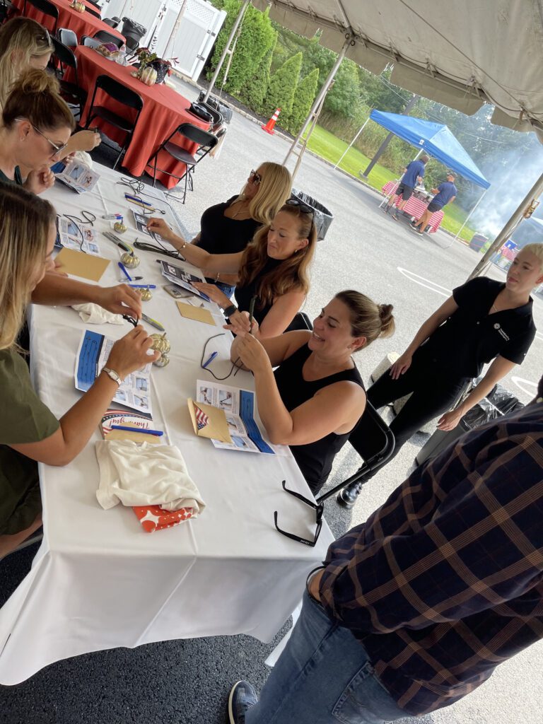 Group of people sitting at a table outdoors working on a team building activity with various materials during a corporate charitable activity.