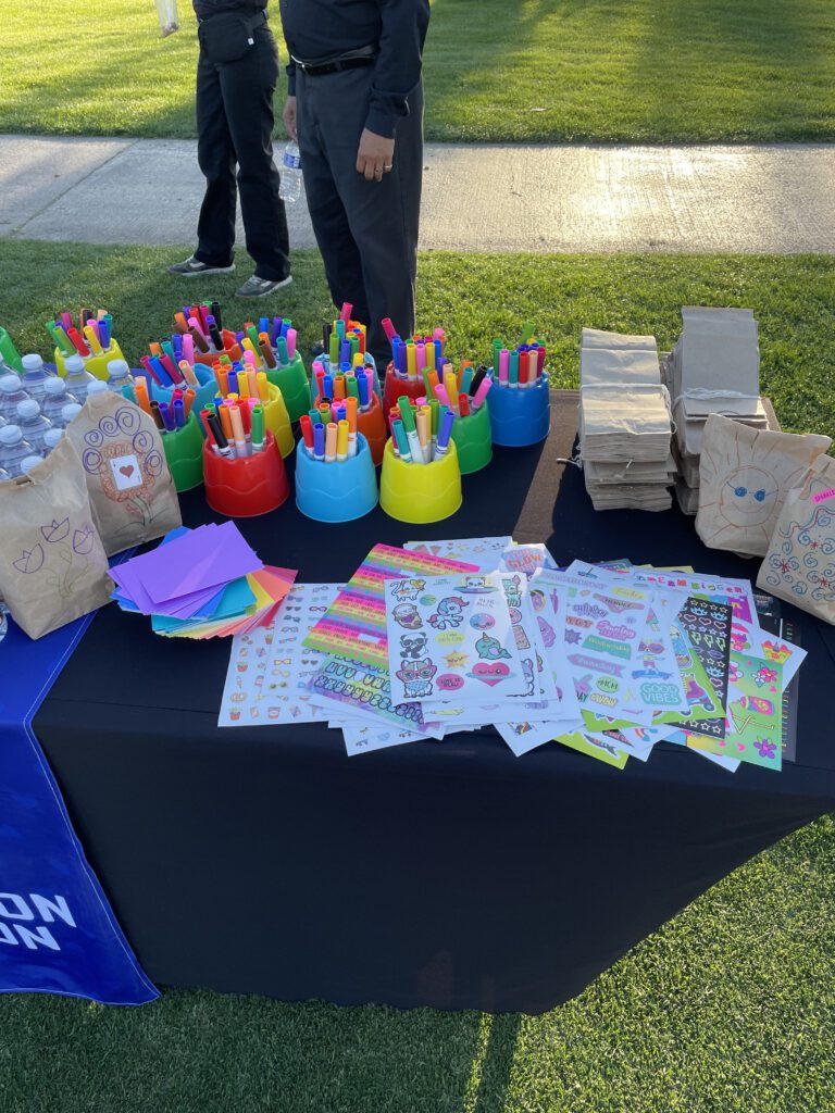 Table set up with colorful markers, stickers, and brown paper bags ready to be decorated during a corporate charitable team building event.