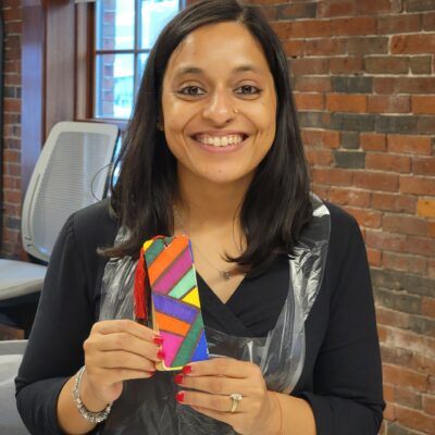 Smiling participant proudly displays a colorful, hand-painted bookmark during a team building activity for Little Team Library. The event encourages collaboration and creativity as teams build and decorate Little Free Library kits, sharing stories and literary inspirations to promote community literacy.