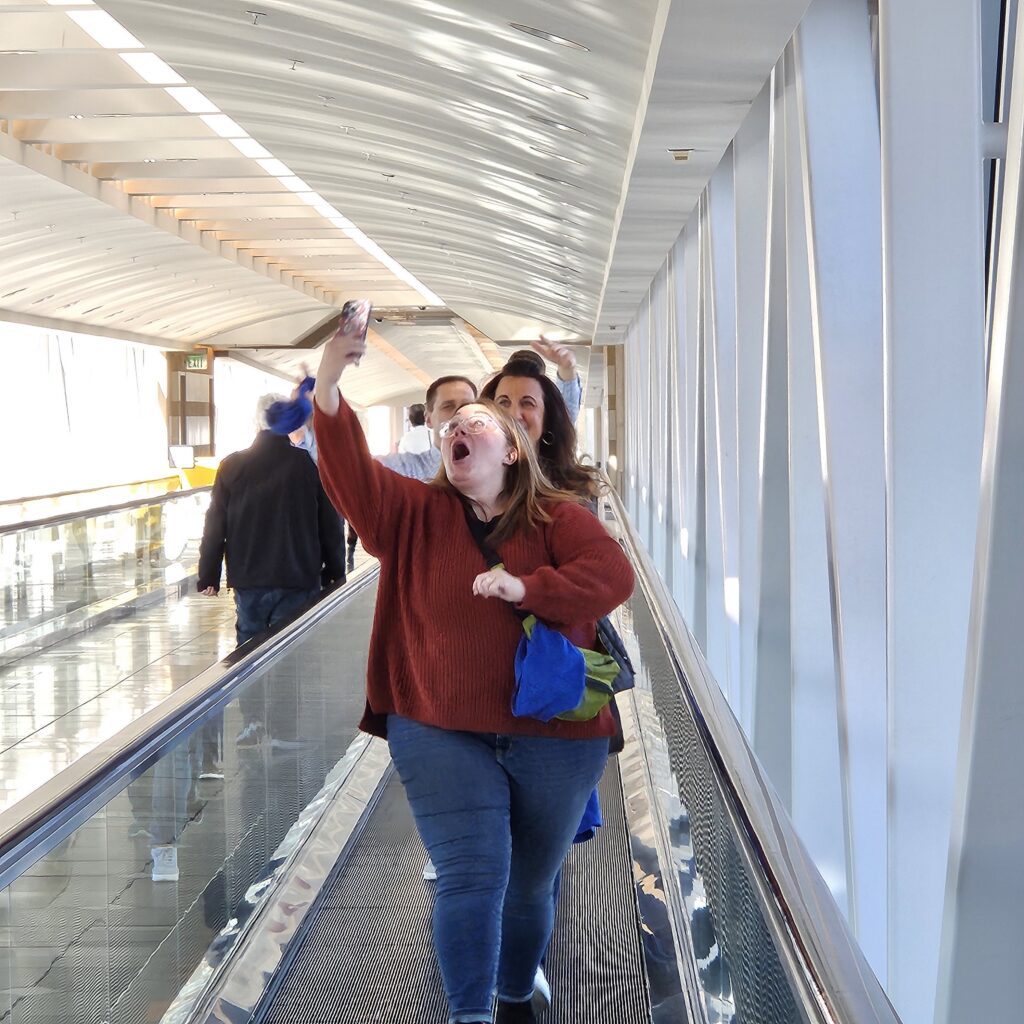 A group of participants on a moving walkway during a team building event, with one person enthusiastically taking a selfie.