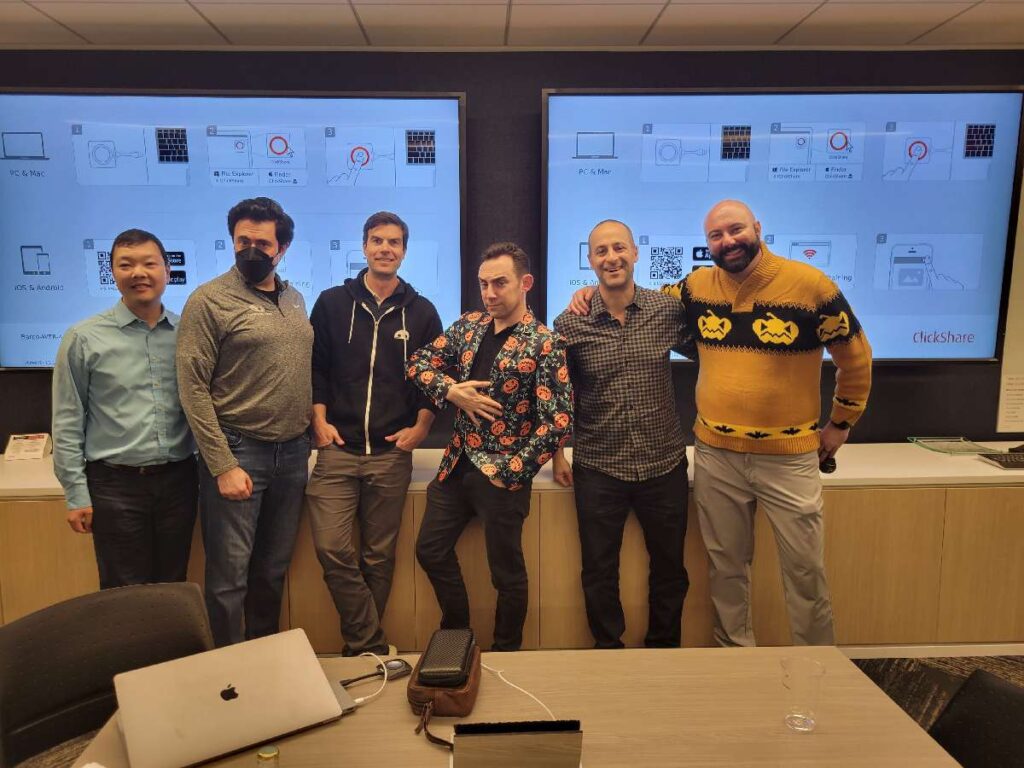 Team members look at their watches, adding a playful sense of urgency during the Monster Mash Dash scavenger hunt, surrounded by Halloween-themed decorations.