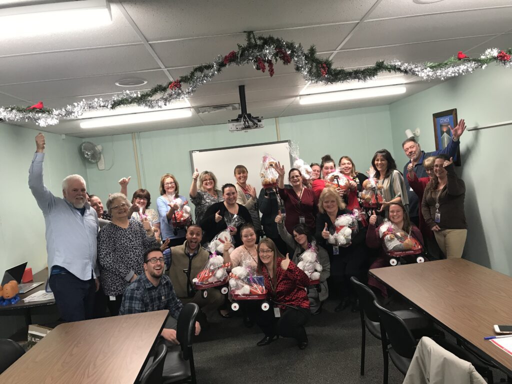 Team members proudly display gift baskets prepared during a holiday-themed team building activity focused on giving back.