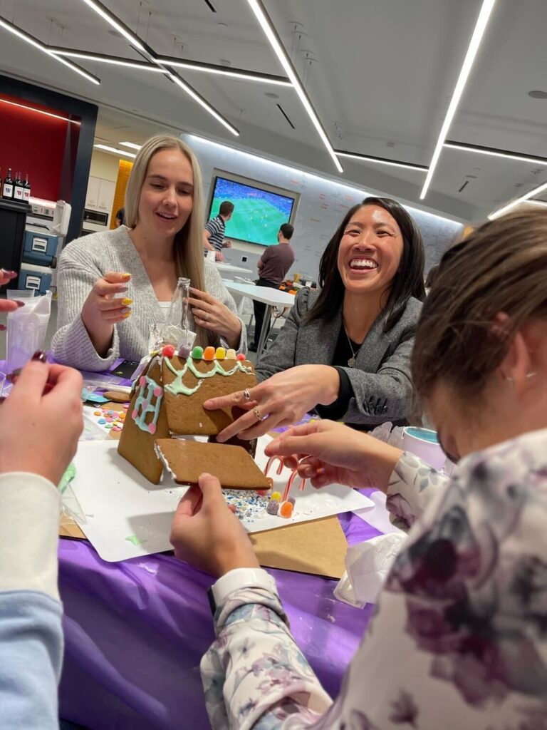 Team members enjoy decorating a gingerbread house during a festive team building activity at the holiday event.