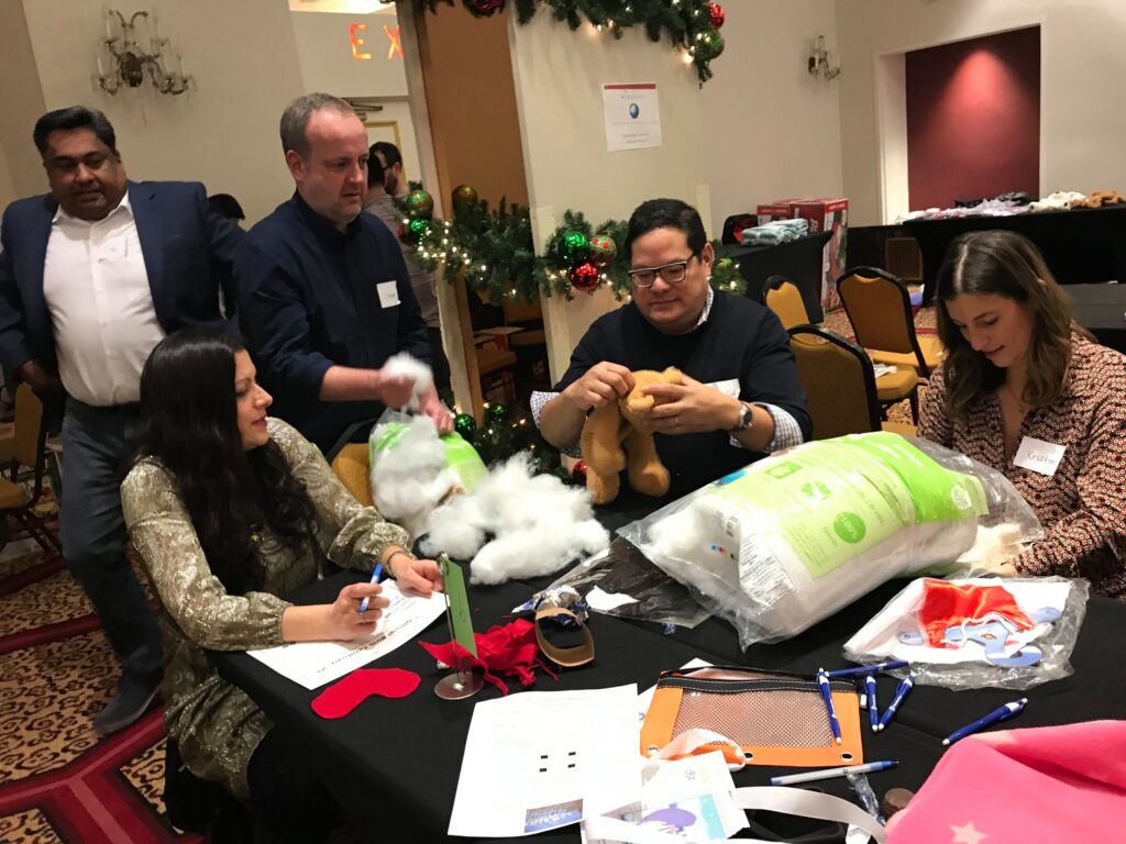 Team members collaborate to stuff teddy bears during a holiday team building activity focused on creativity and giving back.