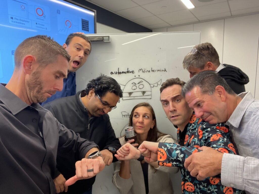 Team members gather in front of a screen after completing the Monster Mash Dash scavenger hunt, celebrating their Halloween-themed team building event.