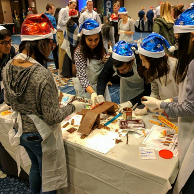 Team members wearing festive hats collaborate to build an edible holiday creation during a fun-filled team building challenge.