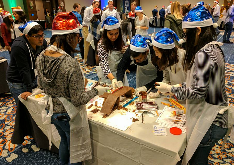 Team members wearing festive hats collaborate to build an edible holiday creation during a fun-filled team building challenge.