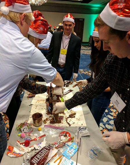 Team members wearing festive hats compete at a chocolate challenge during a holiday team building event.