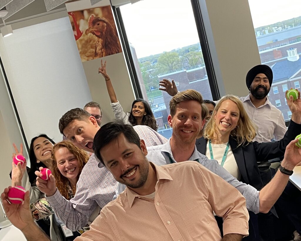 A group of colleagues smiling and holding colorful objects, clearly enjoying a fun and energetic moment during a team building event.