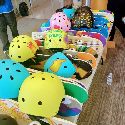 Colorful skateboards and helmets decorated for a charitable team building event. Participants design and assemble skateboards to be donated to children's charities, promoting creativity, teamwork, and community impact.