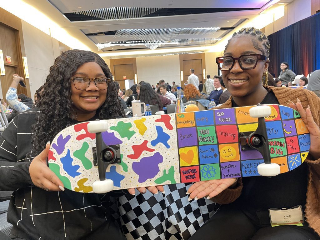 Two participants proudly display their colorful and creatively decorated skateboard, made during the Just Roll With It charitable team building event.