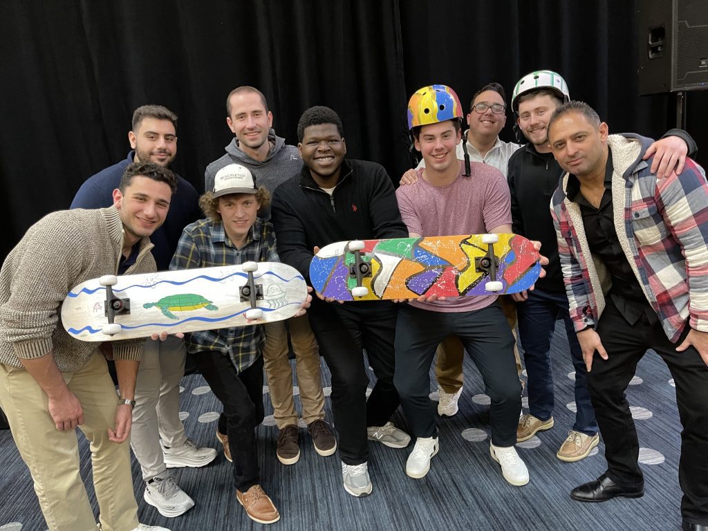 A team proudly showcasing their custom-designed skateboards and helmets created during the Just Roll With It – Charitable Skateboard Build team building event.