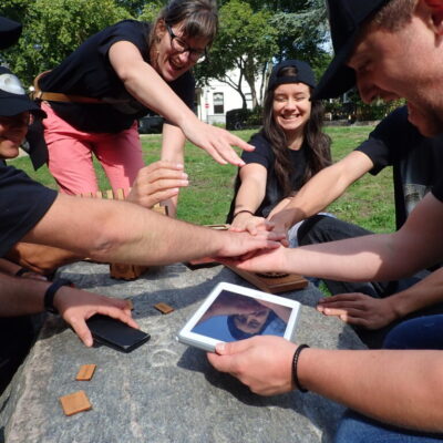 A group of participants enthusiastically working together on a tablet during the Sleuth: The Murder Mystery Scavenger Hunt team building event.