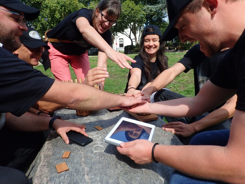 A group of participants enthusiastically working together on a tablet during the Sleuth: The Murder Mystery Scavenger Hunt team building event.