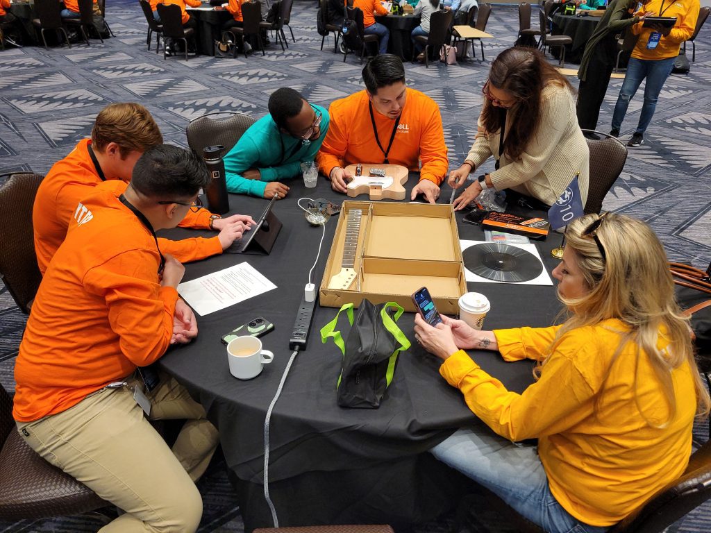 Team members collaborating around a table assembling an electric guitar during the Charity Guitar Build team building event.