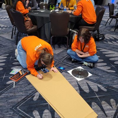 Two team members focused on decorating a cardboard guitar case at the Charity Guitar Build team building event, showcasing creativity and collaboration.