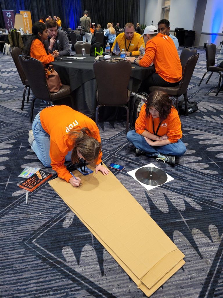 Two team members focused on decorating a cardboard guitar case at the Charity Guitar Build team building event, showcasing creativity and collaboration.