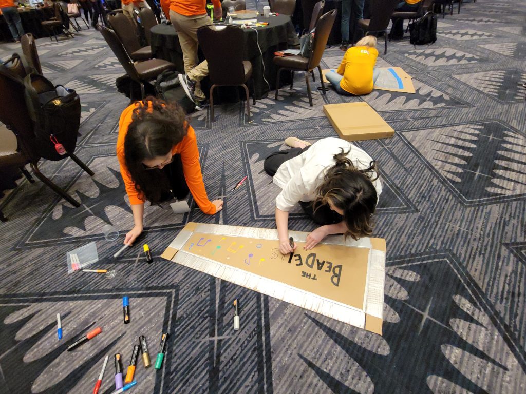 Two participants decorating a cardboard guitar case with colorful designs, adding a personal touch during the Charity Guitar Build team building event.