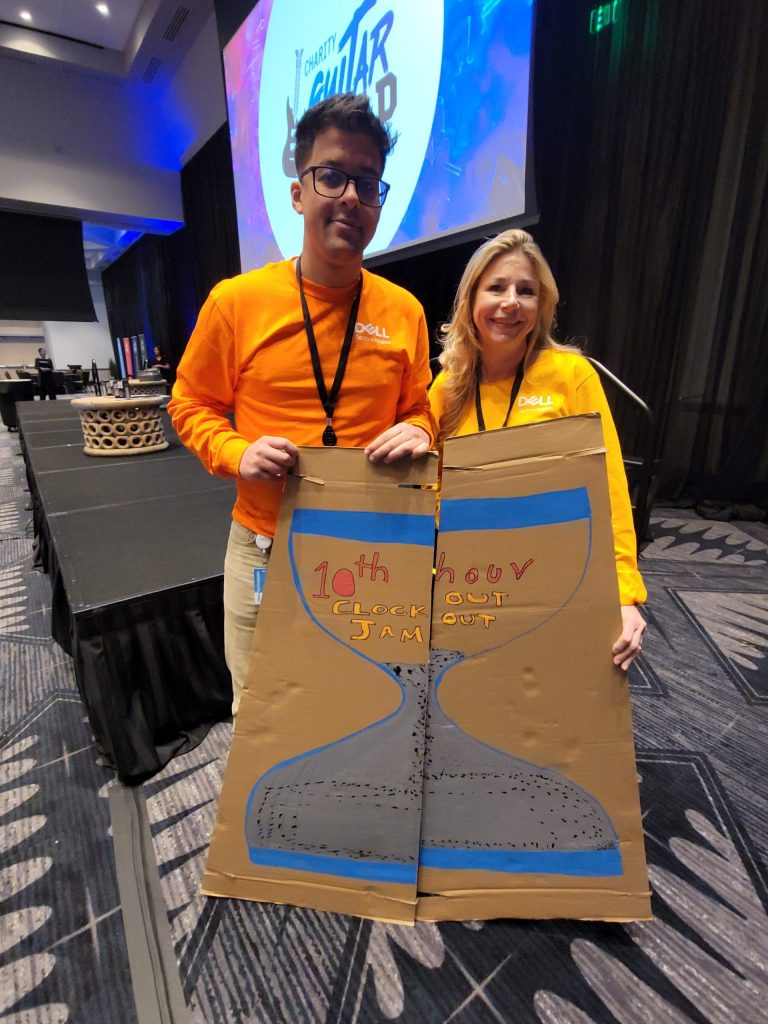 Two team members display their creatively decorated cardboard guitar case with a unique hourglass design during the Charity Guitar Build team building event.