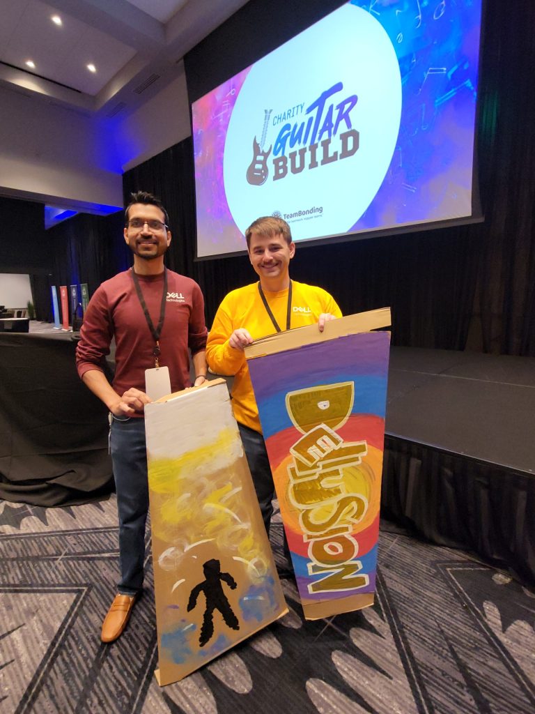 Two participants from the Charity Guitar Build team building event hold their creatively decorated guitar cases, ready to make a difference through music.