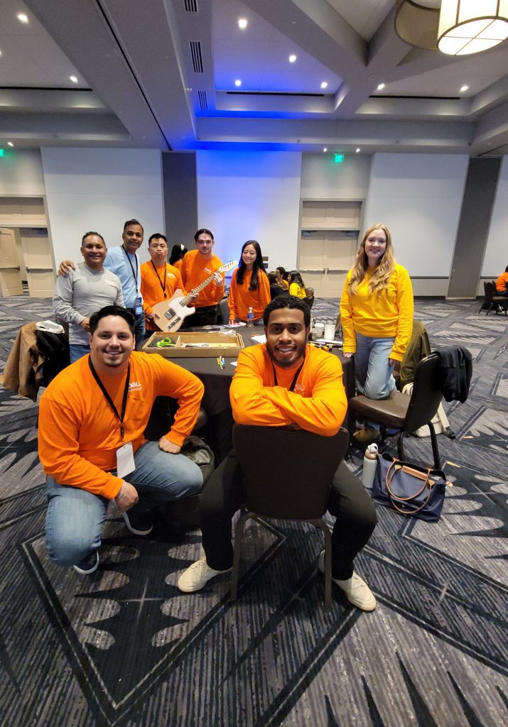 Team poses together during the Charity Guitar Build team building event, proudly showcasing their guitar creation and teamwork.