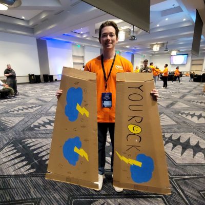 Participant at the Charity Guitar Build team building event holding a decorated cardboard guitar case with the phrase 'YOU ROCK' and colorful designs.