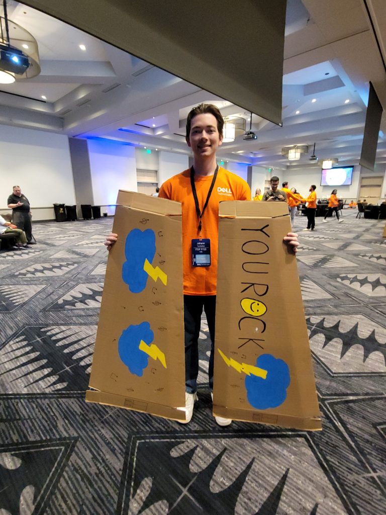 Participant at the Charity Guitar Build team building event holding a decorated cardboard guitar case with the phrase 'YOU ROCK' and colorful designs.