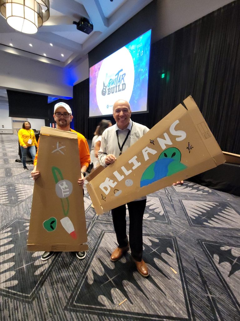 Two participants proudly display their creatively decorated cardboard guitar cases at the Charity Guitar Build team building event.