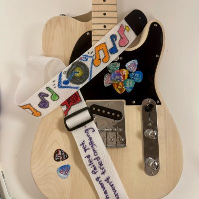 This is a nicely decorated guitar with symbols and an inspirational quote after teams have worked on it during the Charity Guitar Build team building event.