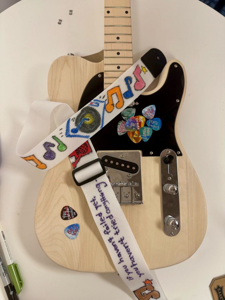 This is a nicely decorated guitar with symbols and an inspirational quote after teams have worked on it during the Charity Guitar Build team building event.