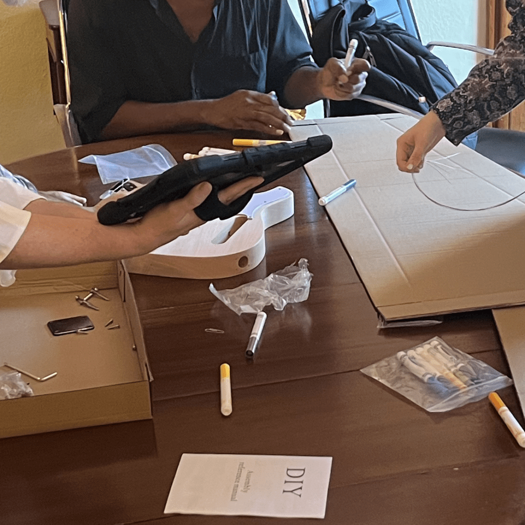 Team members engage in designing custom guitar cases and reviewing instructions during the Charity Guitar Build, contributing creativity and teamwork to support aspiring musicians.