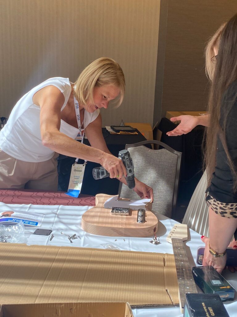 A participant uses a power tool to assemble an electric guitar during the Charity Guitar Build team building event.