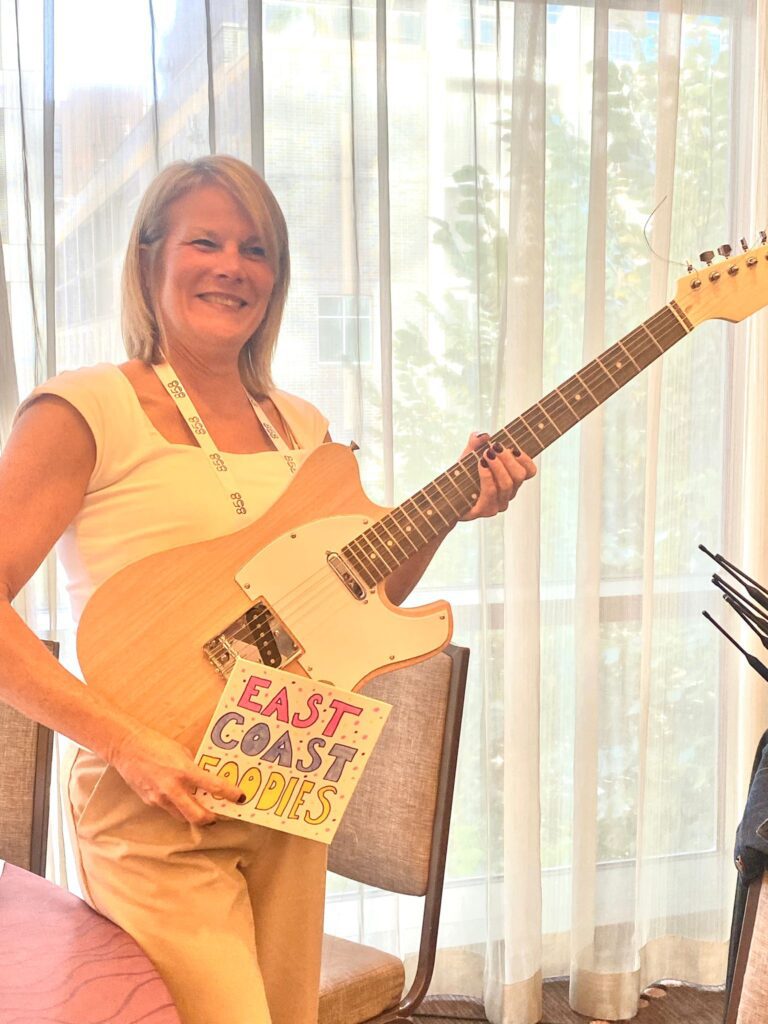 A participant proudly displays a completed electric guitar during the Charity Guitar Build team building event, ready for donation.