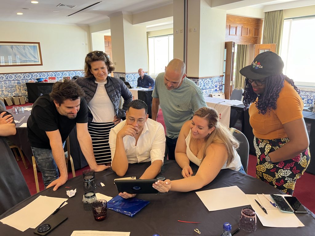 Team building activity focused on human skills training. A group gathers around a tablet, collaborating and strategizing to complete a challenge, reinforcing teamwork, communication, and problem-solving skills.