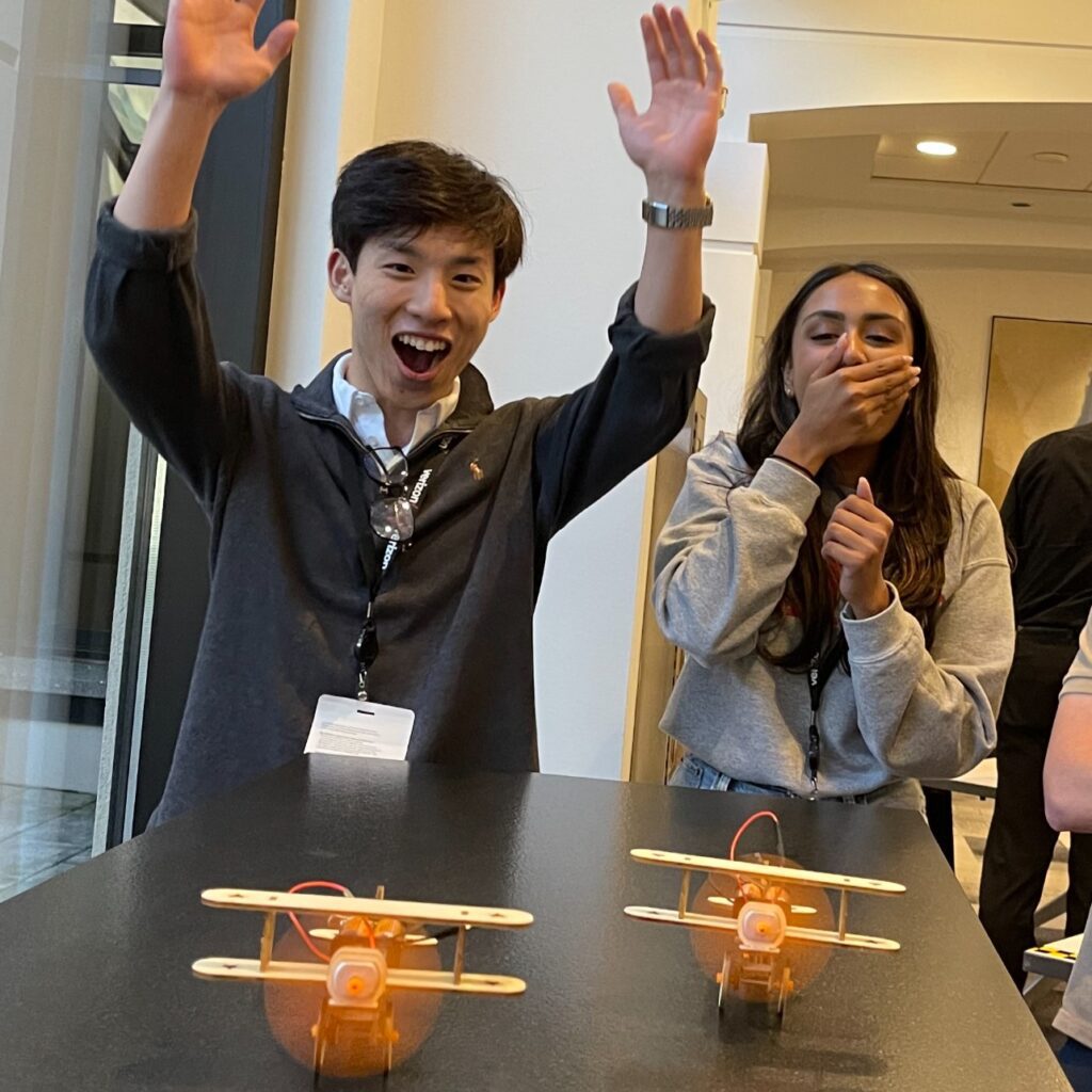 Two participants celebrating and smiling after successfully assembling and testing their miniature airplanes during the STEM Speedway team building activity, showcasing excitement, teamwork, and hands-on learning with STEM kits.