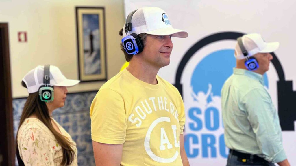 A group of participants in a Sound Crowd event stand attentively while wearing noise-cancelling headphones. They are participating in a team building event that focuses on non-verbal communication.