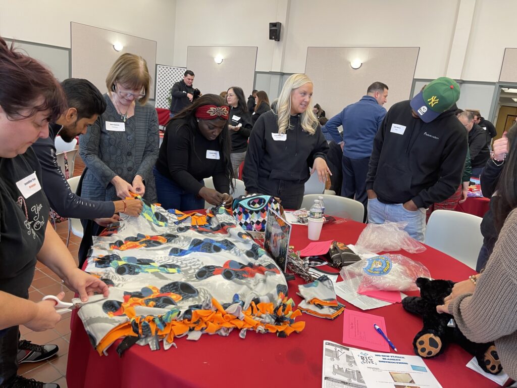 Team members actively collaborate to create cozy blankets during a Hope for the Holidays team building event, contributing to gift baskets that will bring warmth and joy to seniors this holiday season.