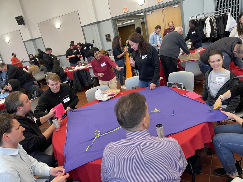 Team members collaborate on crafting a fleece blanket during a charitable team building event, contributing to donations for a good cause as part of the Hope for the Holidays program.